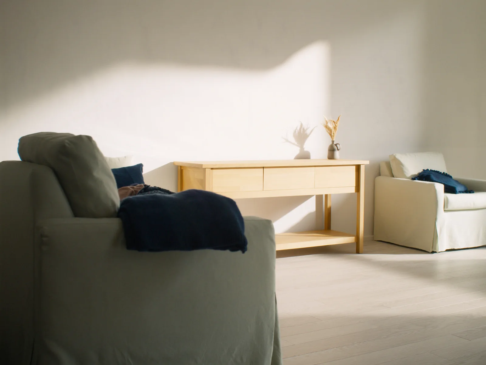 A quiet waiting area: linen armchairs, a pale oak console and a folded navy throw in afternoon light