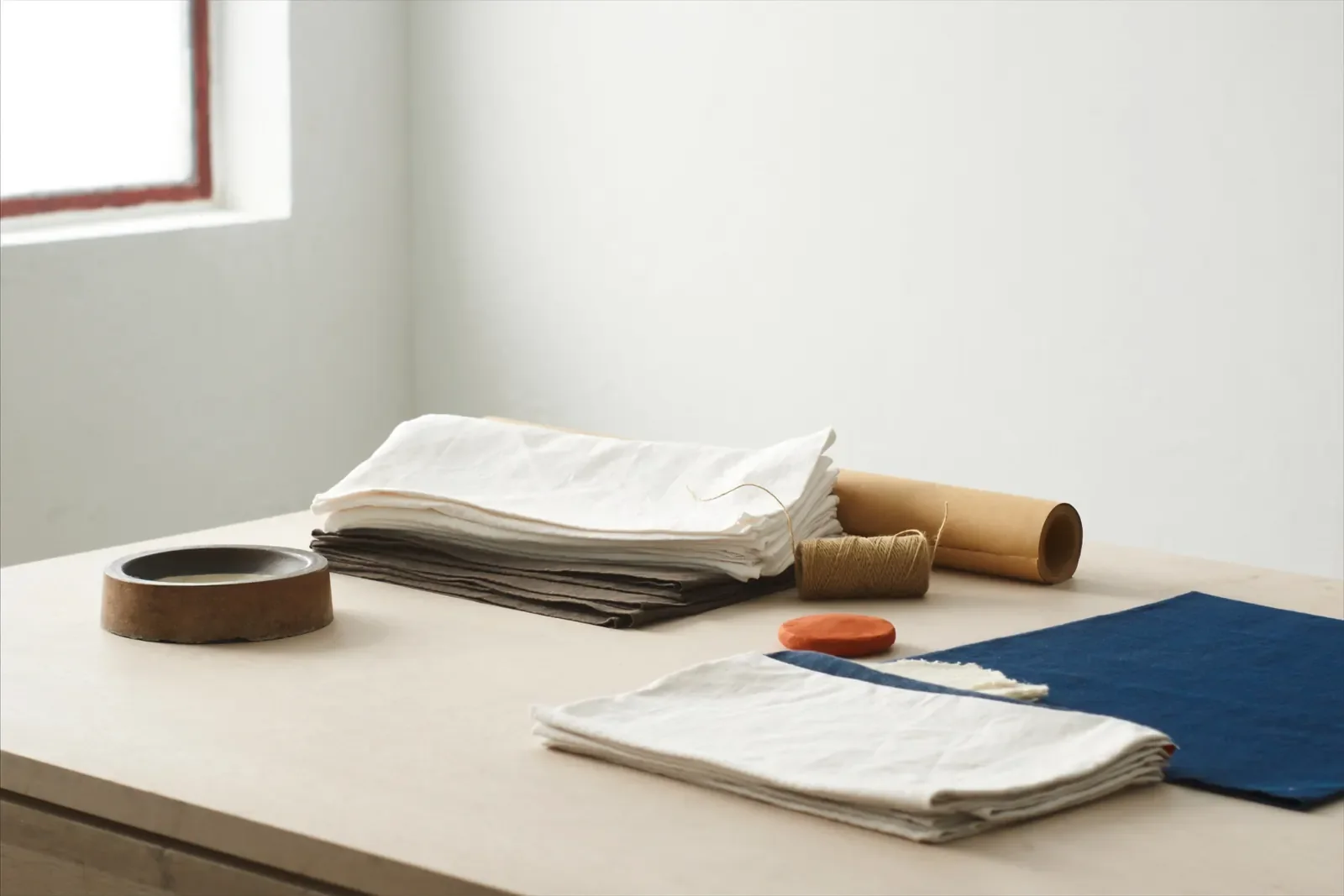 A maker’s table with folded linen, a roll of kraft paper and twine in window light